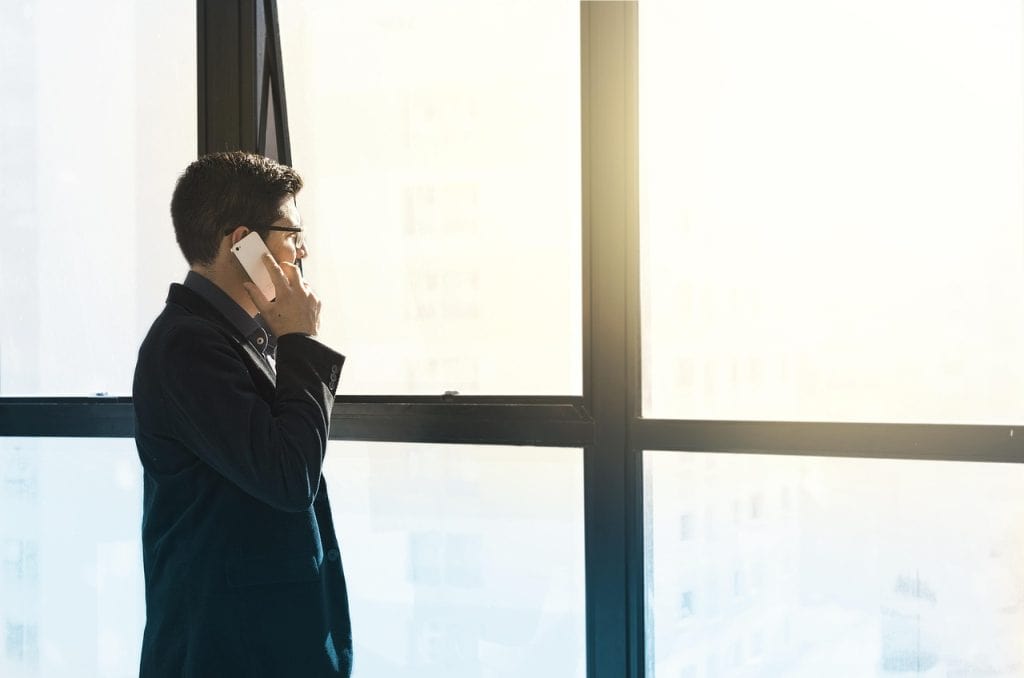 Stable, confident businessman on a call looking out a large window in a modern office setting.